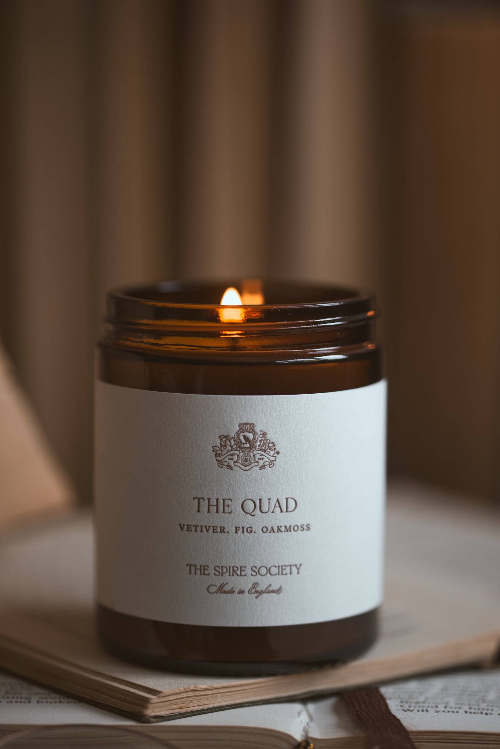 Candle in a jar labeled 'The Quad' from 'The Spire Society' on a blurred background